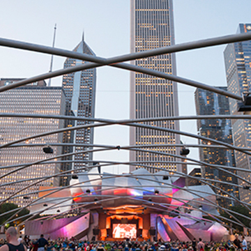 Millenium park, curved beams covering its stage glowing at the center, skyscrapers behind it